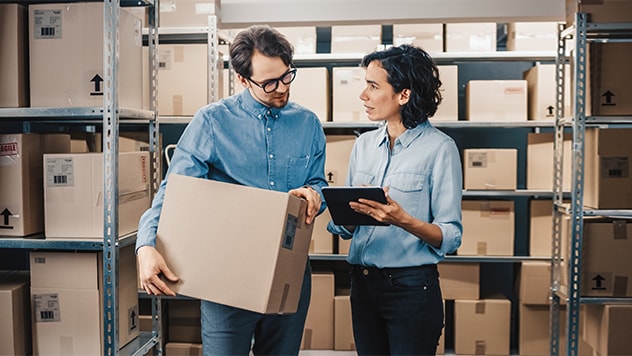Twee mensen die in een magazijn lopen, een van hen draagt een doos