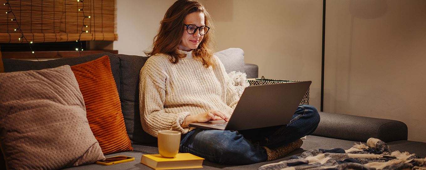 Jonge vrouw op de bank met een laptop in wintersfeer met lampjes