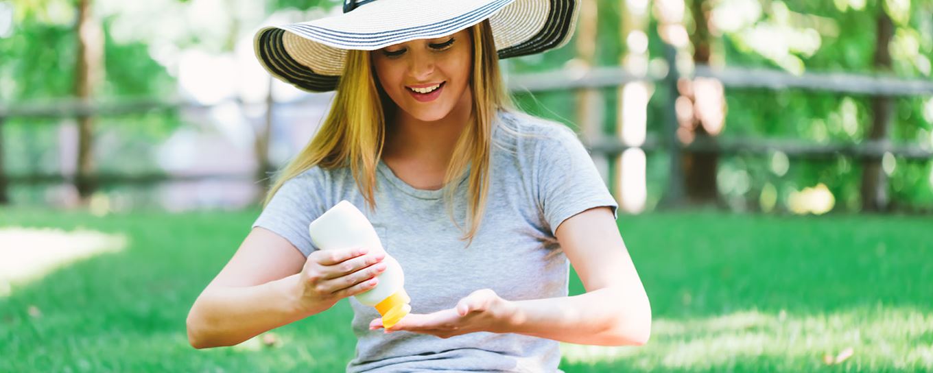 Vrouw met hoed op spuit zonnebrandcreme in haar hand
