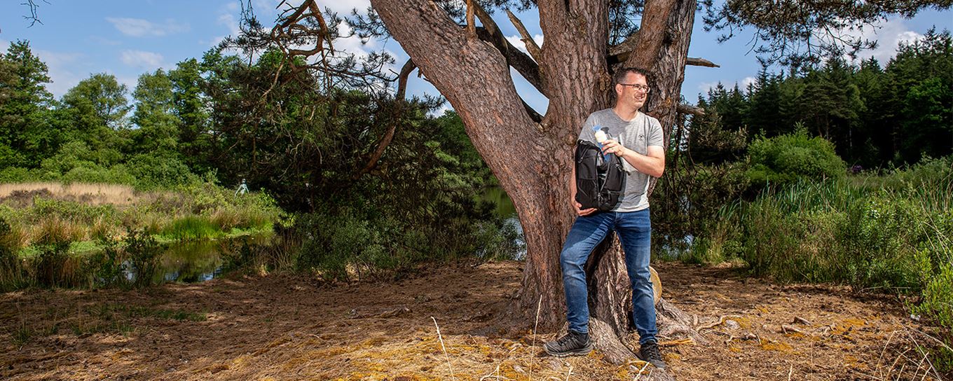 een man van middelbare leeftijd staat met zijn rugzak in de schaduw onder de boom uit te rusten
