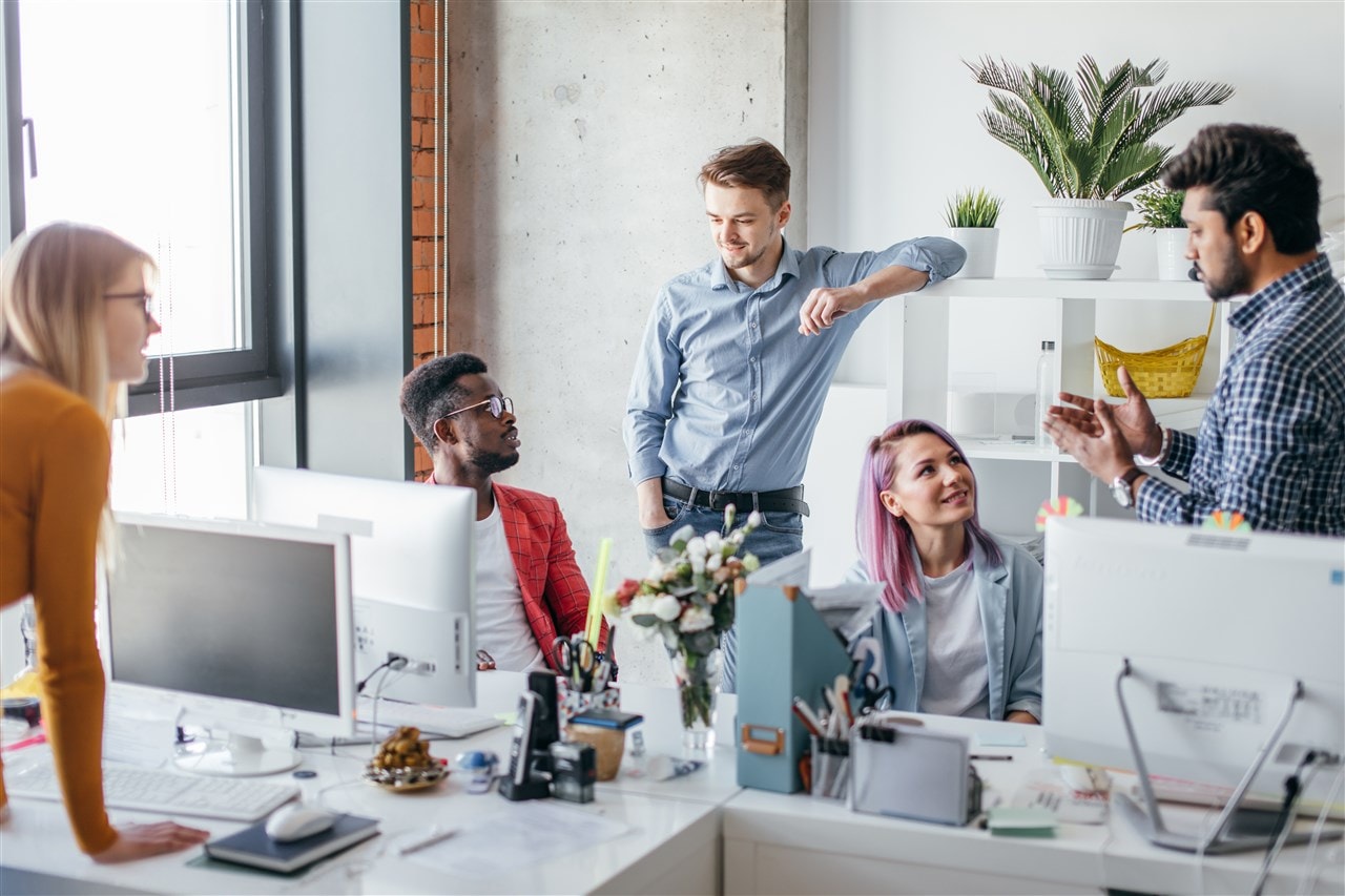 vijf collega's bij hun bureau twee zitten drie staan